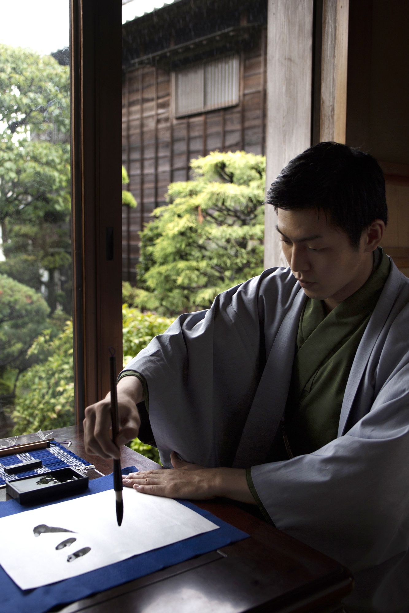 筆で日本語の文字を書く練習をする着物姿の男性
